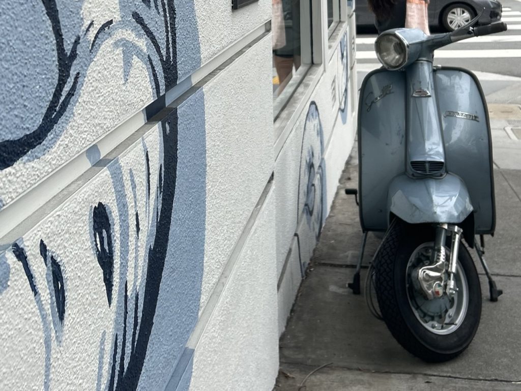 A silver-blue, 1969 Lambretta Li125 parked on a city street next to a blue, grey, and white mural ©Kate Dana