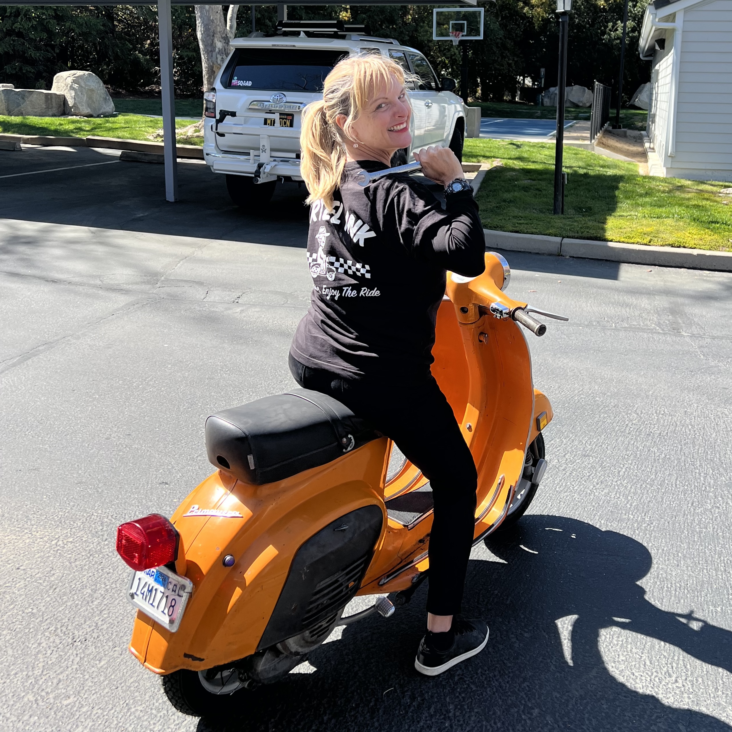 A person holds a wrench while sitting on a 1973 Vespa photo © Kate Dana